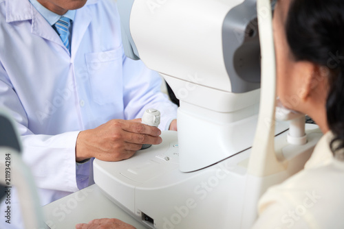 Tableau sur toile Crop shot of doctor controlling special machine while examining eyesight of pati
