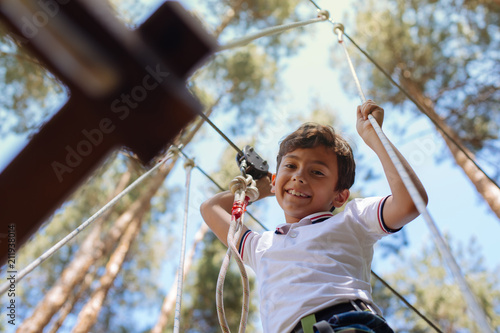 No acrophobia. Cute preteen boy looking down and smiling while moving along trails at an adventure park