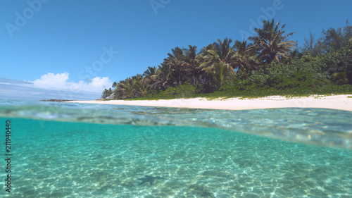 HALF UNDERWATER: Tranquil turquoise ocean washes the idyllic white sand beach. © helivideo