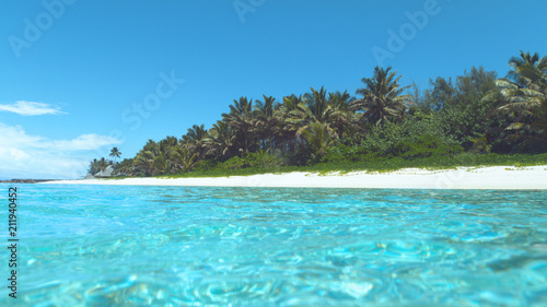 Glassy ocean water glistens in the bright summer sunshine near tropical island