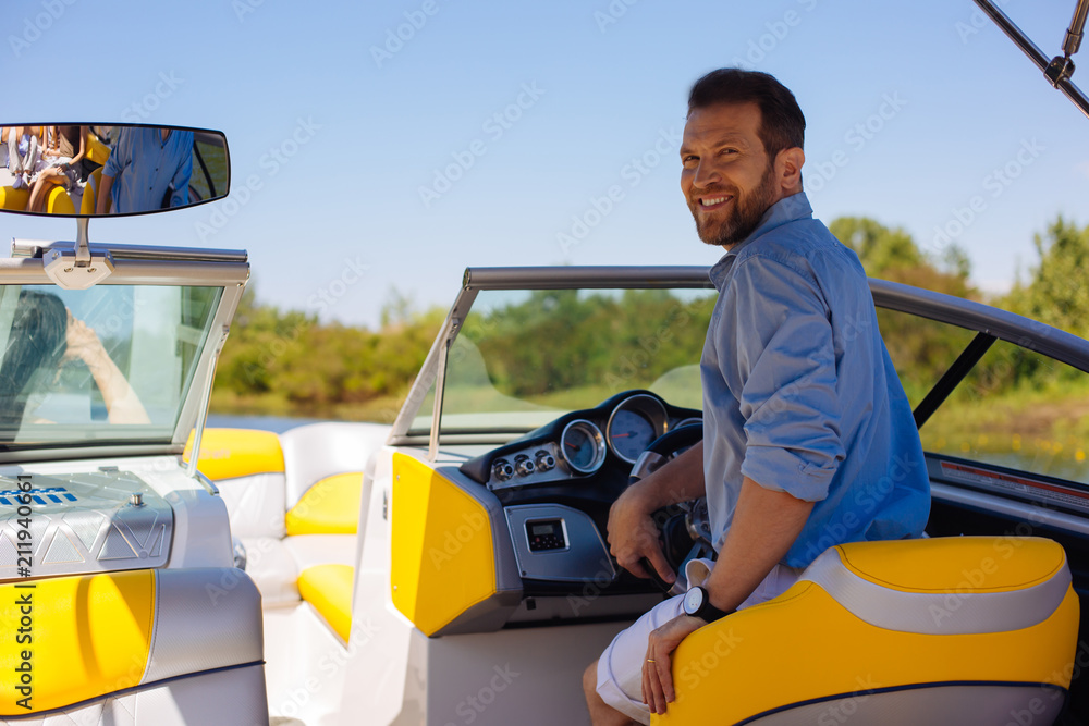 Proud owner. Pleasant young man posing behind a steering wheel of a yacht and smiling, being proud of his purchase