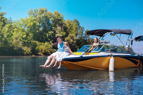 Pleasant chat. Loving young father and his beloved little daughter sitting on the bow of the boat and chatting together
