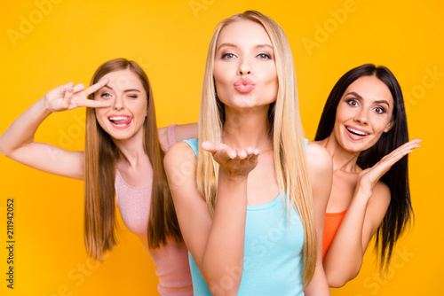 Dream inspiration affection concept. Portrait of foolish playful girls showing different emotions blowing kiss gesturing tongue out showing two fingers isolated on bright yellow background