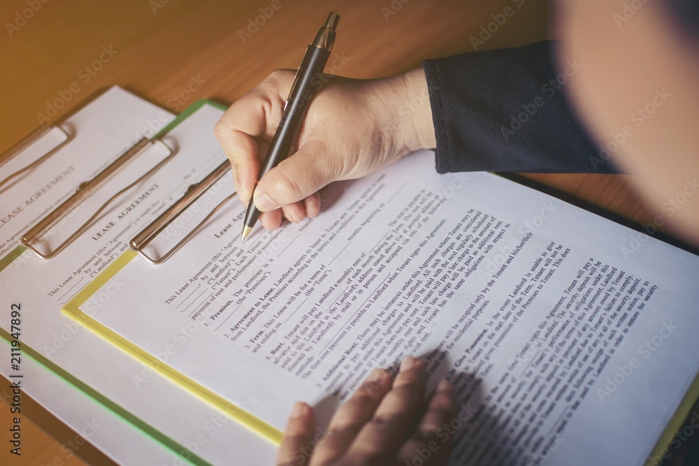Closeup of new homeowner signing a contract of house sale or mortgage papers with a wooden toy house on the document. Suitable for real estate concept. Closeup of new homeowner signing a contract of house sale or mortgage papers with a wooden toy house on the document. Suitable for real estate concept.