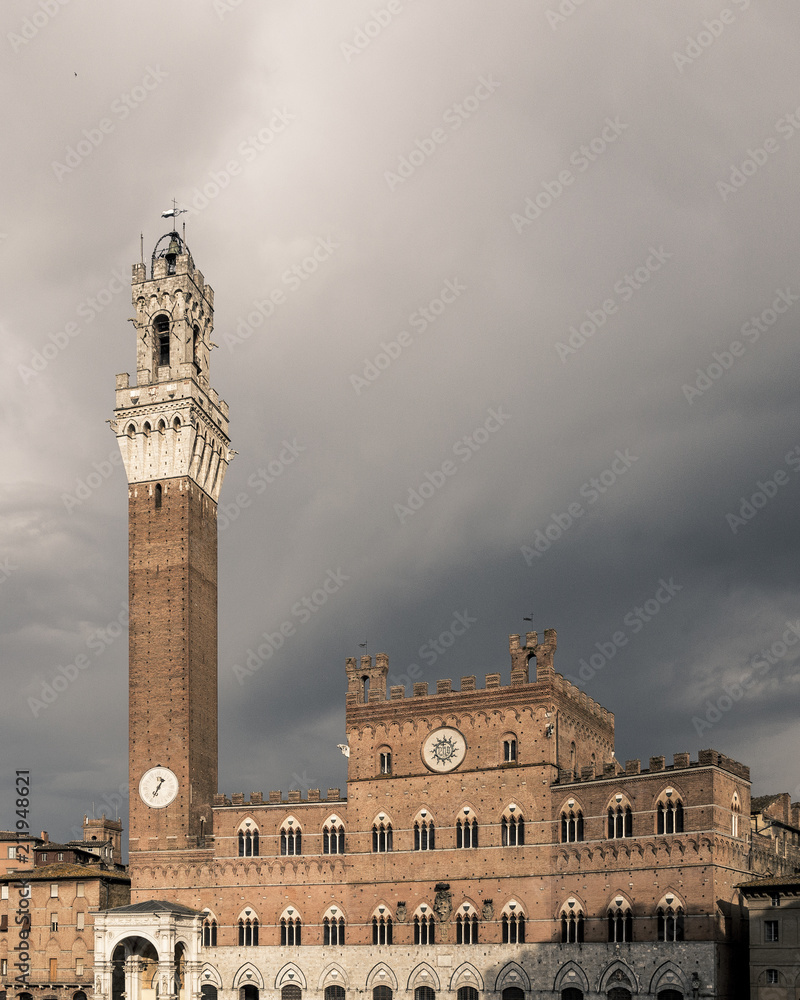 Palazzo Pubblico and Mangia tower against overcast sky in the historic center of Siena, Italy