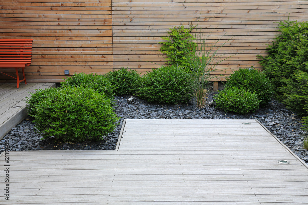 Moderner Gartenbau und Terrassengestaltung: Terrasse aus Holz und Pflanzen  im pflegeleichten Schotterbett vor einer Holzwand Stock Photo | Adobe Stock