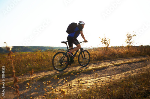 Fototapeta Naklejka Na Ścianę i Meble -  Male cyclist with backpack driving by rural dirt road outdoors