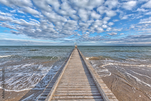 Ein Steg führt ins Mittelmeer am Strand von Lido di Jesolo, Italien, mit einem prachtvollen Wolkenhimmel und schönen blau-türkisen Farben photo