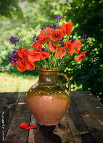Fototapeta Naklejka Na Ścianę i Meble -  Clay vase with flowering poppies on a wooden table. Traditional Ukrainian bouquet.