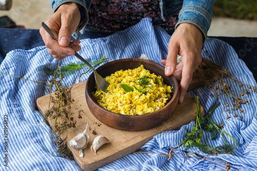 Woman hands holds vegan raw cauliflower rice porridge mixed and dressed with turmeric powder, spices and green herbs. Raw vegan vegetarian healthy food. Raw foodist lunch or dinner photo