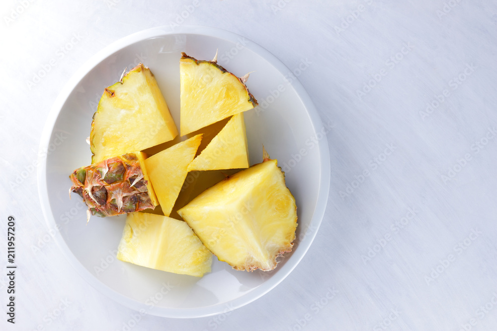 Pieces of pineapple on a white plate, pineapple on a white background top view, salad of tropical fruits for breakfast, vegetarian food, copy space Pieces of pineapple on a white plate, pineapple on a white background top view, salad of tropical fruits for breakfast, vegetarian food, copy space