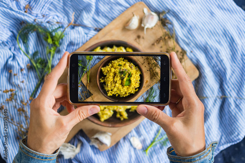 Woman hands take smartphone food photo of cauliflower vegan rice. Phone food photography for social media or blogging in popular and trendy top view style. Raw vegan vegetarian meal concept.
