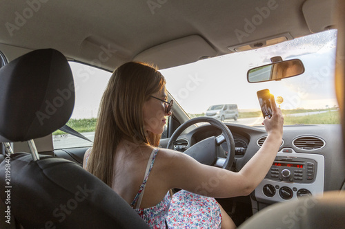 Young girl driving a car and taking selfie by mobile phone