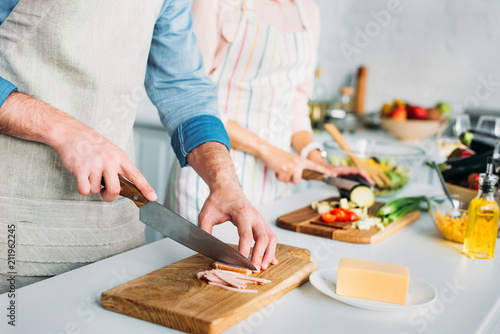 cropped image of couple cooking and cutting vegetables with meat in kitchen