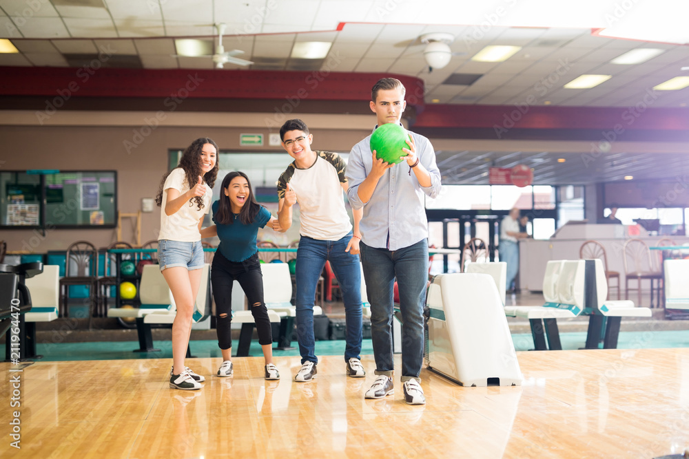 Fototapeta premium Boy Ready To Go Bowling While Friends Cheering In Club