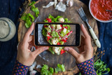 Woman hands take smartphone food photo of cauliflower vegetables salad. Phone food photography for social media or blogging in popular and trendy top view style. Raw vegan vegetarian meal concept.