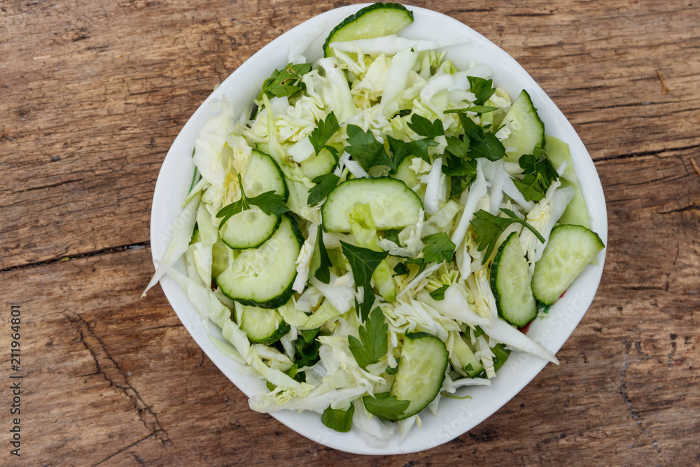 Spring vegan salad with cabbage, cucumber, green onion and parsley on wooden table. Top view Spring vegan salad with cabbage, cucumber, green onion and parsley on wooden table. Top view