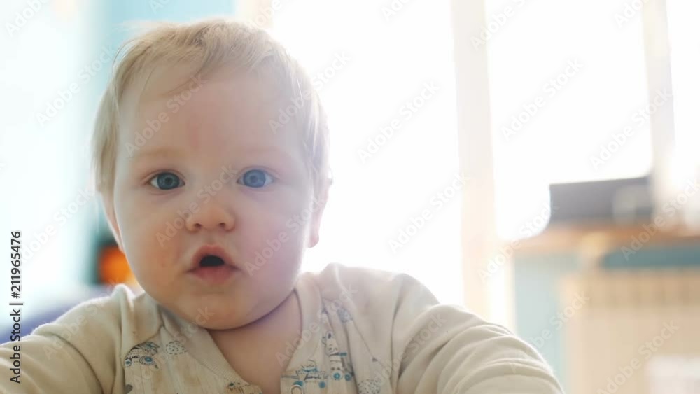 Portrait of healthy serious conscious pretty adorable newborn baby boy standing near sofa and looking at camera bright day light on background chubby cheeks reaching arms blue eyes sweet infant home Portrait of healthy serious conscious pretty adorable newborn baby boy standing near sofa and looking at camera bright day light on background chubby cheeks reaching arms blue eyes sweet infant home