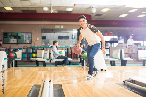 Teen Boy Throwing Ball While Practicing Bowling Game In Club
