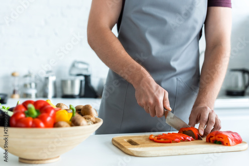 cropped shot of man in apron cutting vegetables in kitchen
