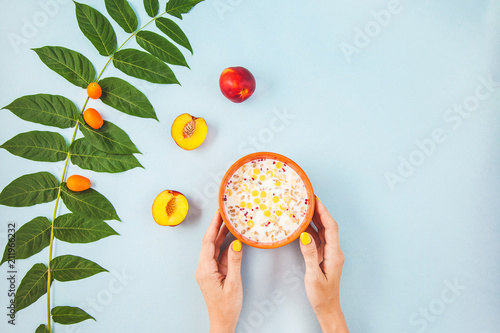 morning breakfast, girl's hands holding muesli, fruit , peaches on blue background with green leaves Copyspace photo
