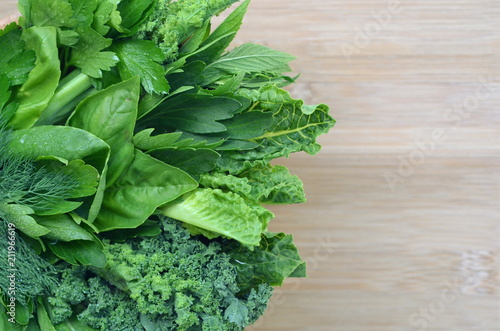 Top view flat layout of fresh culinary herbs and green leafy vegetables on a bamboo cutting board with copy space. Background for nutrition, food, health, cooking, diet and weight loss themes.
