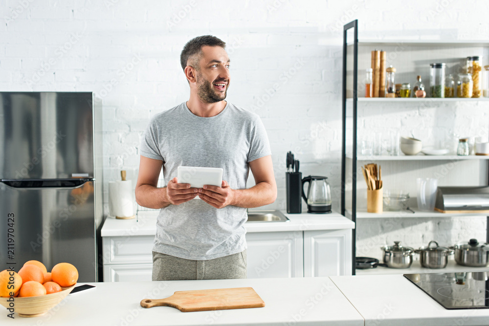 smiling man holding digital tablet near table on kitchen smiling man holding digital tablet near table on kitchen