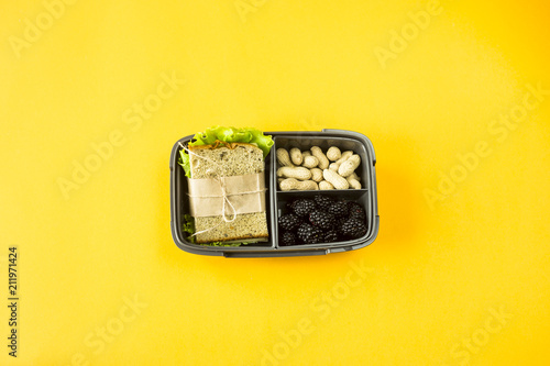 Lunchbox with food - sandwich, nuts and berries on a yellow background. Top view, flat lay,