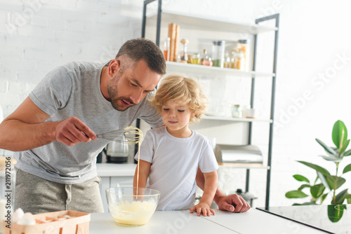 man teaching son making dough in bowl at kitchen