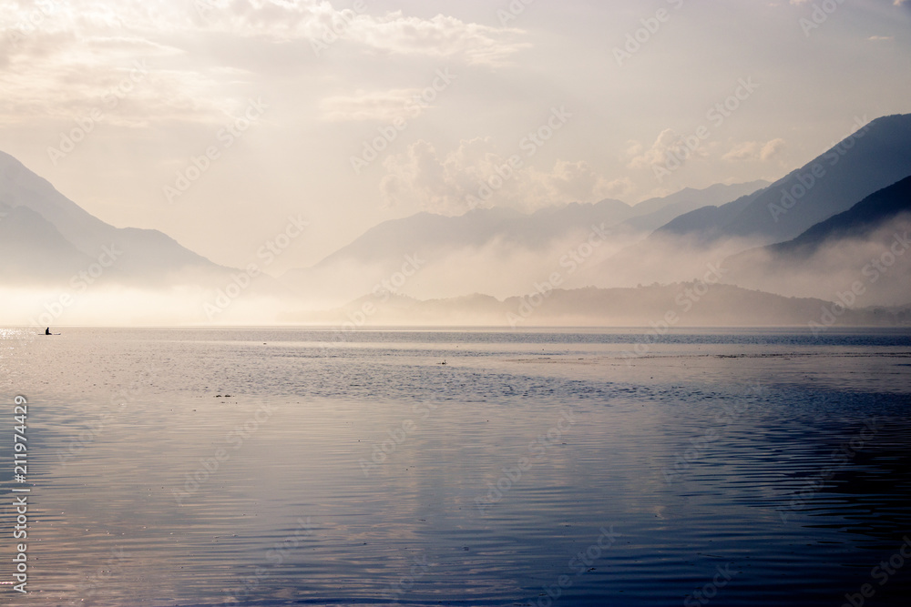 Early morning sunrise on lake Como in Italy. The sun is breaking through as the fog starts to disappear from the surface of the water. After that it is time to wait for the wind to go windsurfing