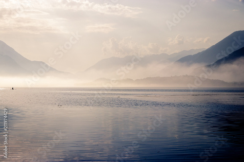Early morning sunrise on lake Como in Italy. The sun is breaking through as the fog starts to disappear from the surface of the water. After that it is time to wait for the wind to go windsurfing