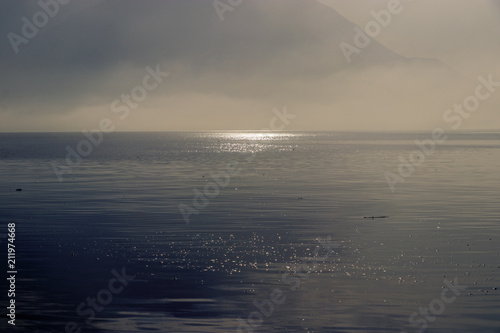 Early morning sunrise on lake Como in Italy. The sun is breaking through as the fog starts to disappear from the surface of the water. After that it is time to wait for the wind to go windsurfing