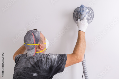 Fotografie Plasterer wearing dust mask polishes a wall with sanding machine