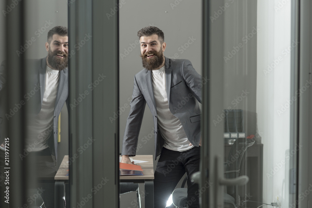 Happy man in casual suit at working place. Bearded man look out room door. Confident businessman in modern office with glass walls. Business and office lifestyle. Confidence and success concept Happy man in casual suit at working place. Bearded man look out room door. Confident businessman in modern office with glass walls. Business and office lifestyle. Confidence and success concept