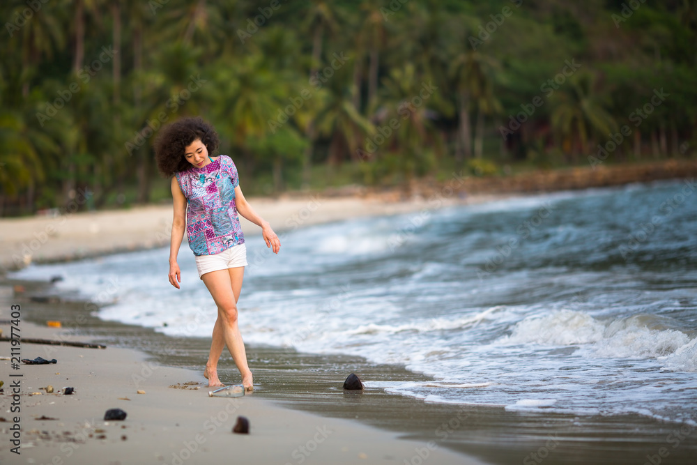 Young mixed race woman walking on along a polluted tropical beach. Environmental problem.