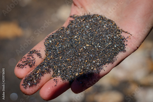 A hand full of black mineral sand from the beach on the island of Elba in the Tuscany, Italy. The sand is reflecting in the sun and has beautiful colors.