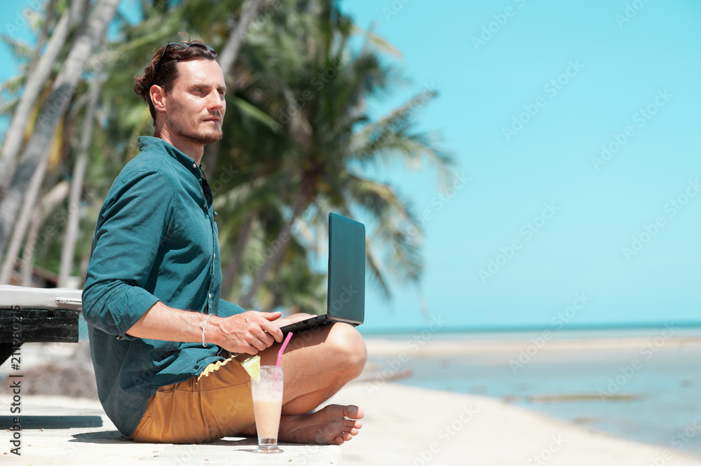 Man freelancer with laptop sitting at the beach