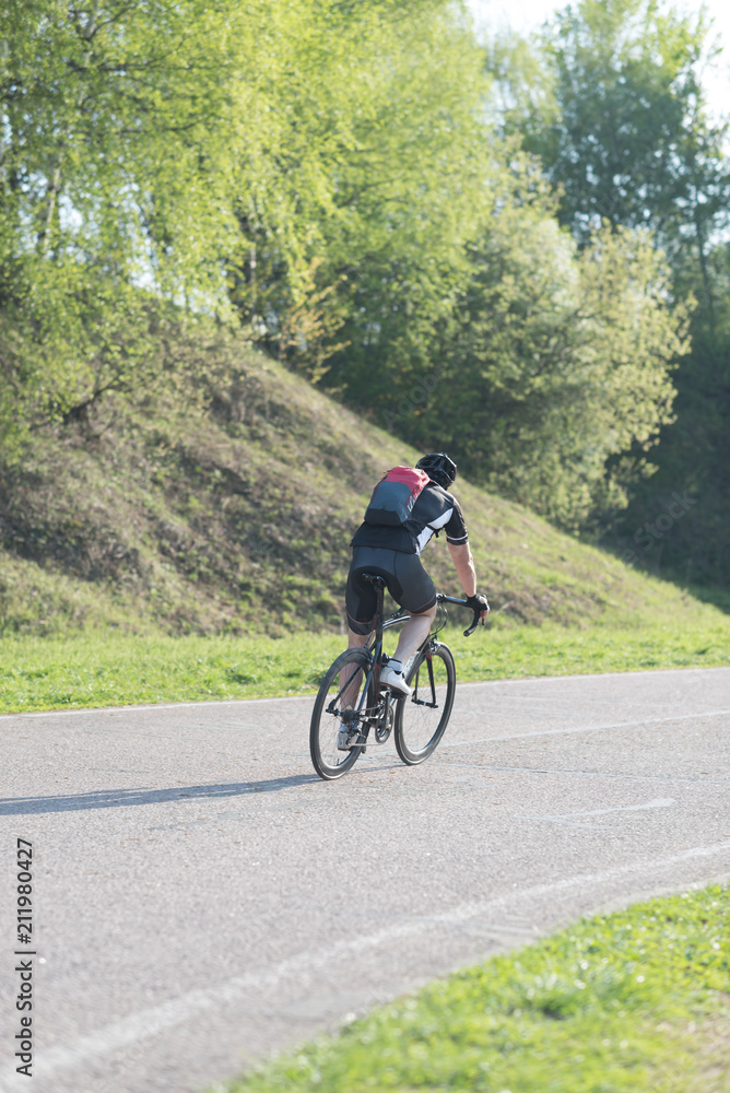 Back of a cyclist with a backpack while riding in the city on a bike. Man in sportswear and a helmet rides the city park.