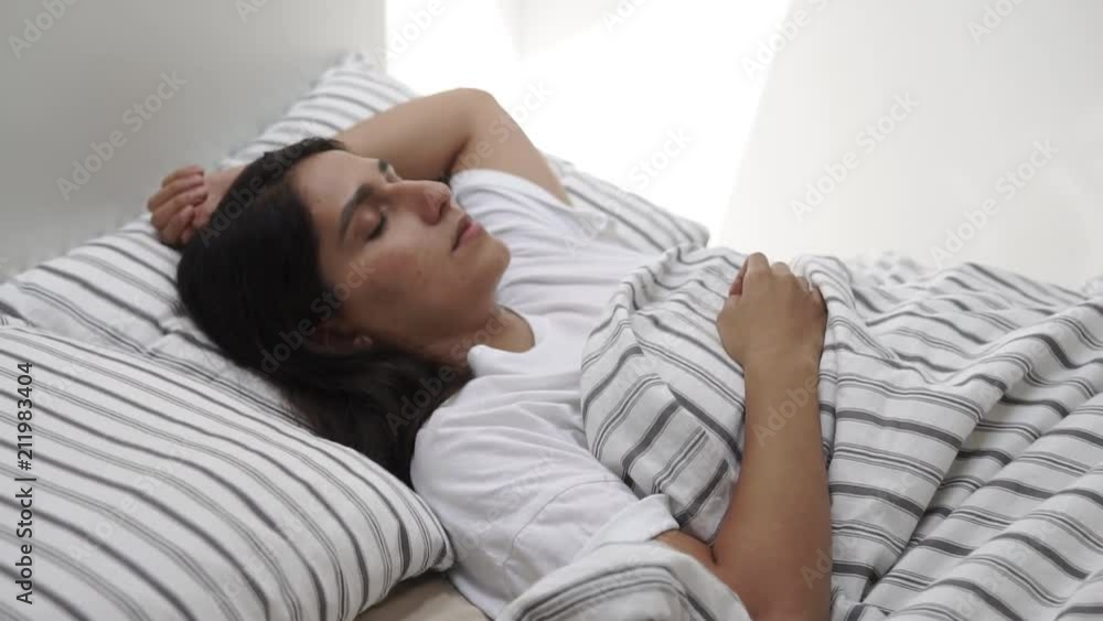 a young and pretty woman lies in a bed with her eyes closed, her head is on the pillow, and the body is covered with a blanket, the woman is sleeping a young and pretty woman lies in a bed with her eyes closed, her head is on the pillow, and the body is covered with a blanket, the woman is sleeping