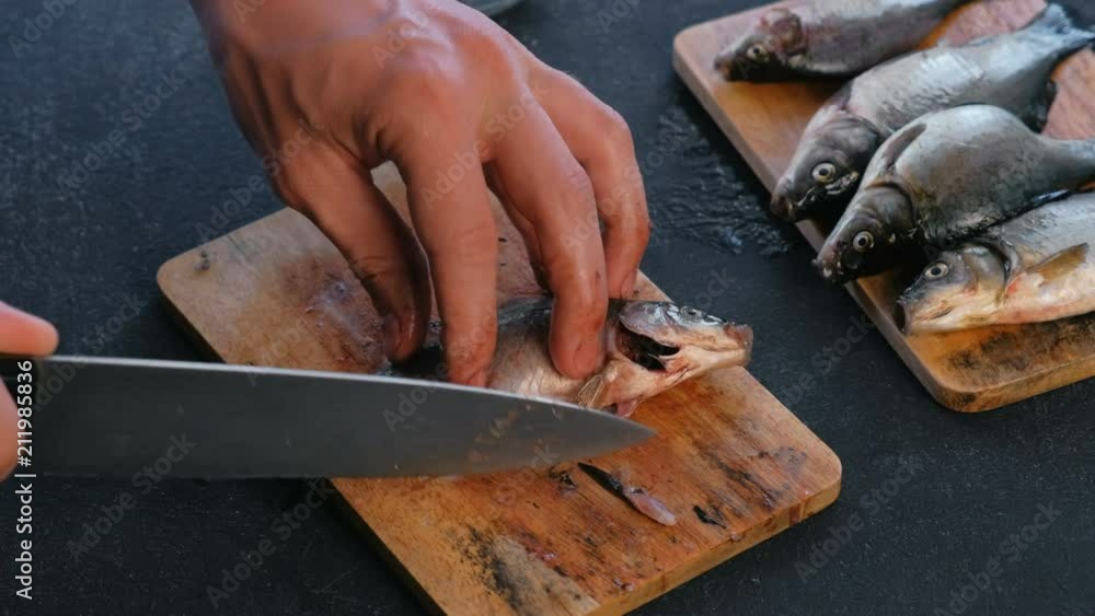 Man cuts the fins of the carp fish on wooden board. Cooking fish. Hands close up. Man cuts the fins of the carp fish on wooden board. Cooking fish. Hands close up.