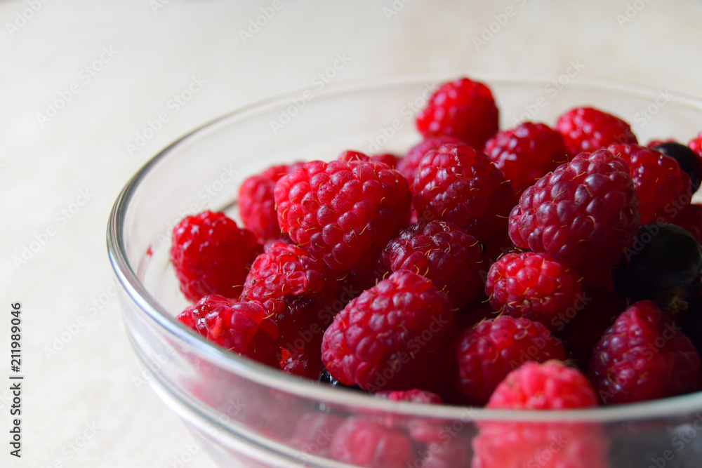 Berries of raspberry and several berries of bilberry are in a glass bowl. Close up, white background Berries of raspberry and several berries of bilberry are in a glass bowl. Close up, white background