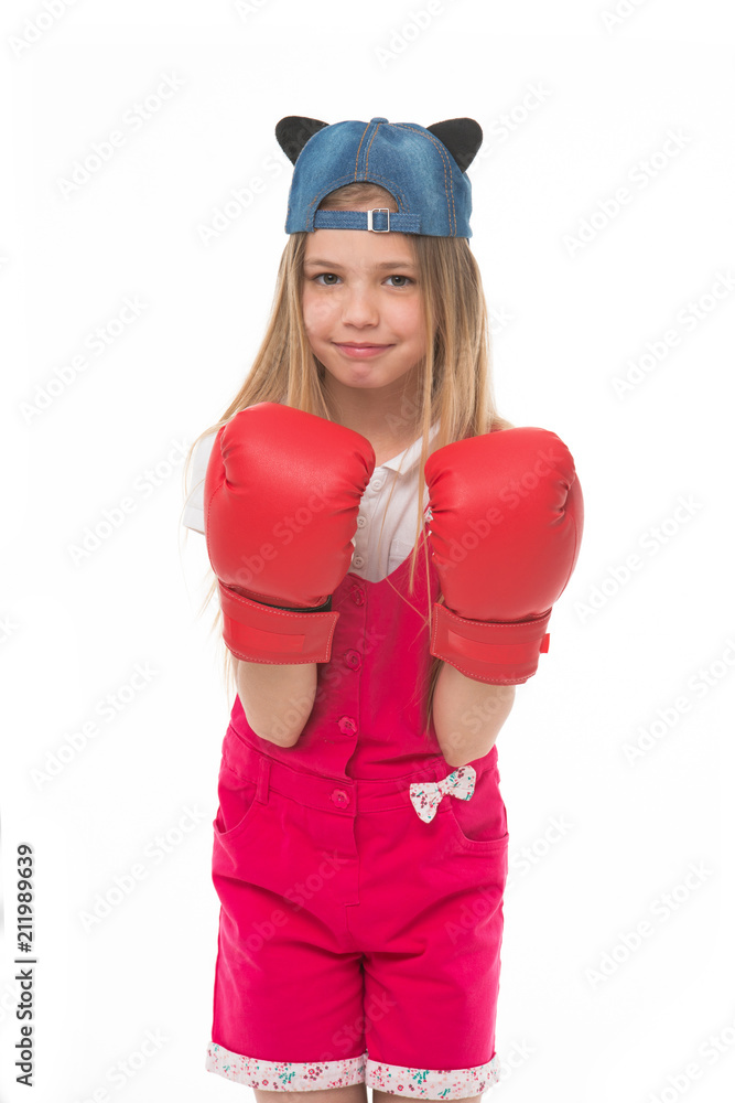 Lovely child wearing huge red boxing gloves. Girl in pink overalls isolated on white background. Kid wearing cute cap with animal ears backwards. Little fighter on training, self defence concept Lovely child wearing huge red boxing gloves. Girl in pink overalls isolated on white background. Kid wearing cute cap with animal ears backwards. Little fighter on training, self defence concept