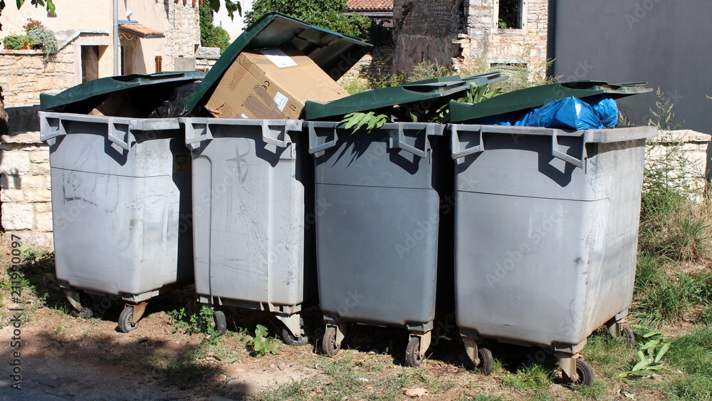 Completely full partially open four gray plastic trash containers with green lids waiting for pickup Completely full partially open four gray plastic trash containers with green lids waiting for pickup