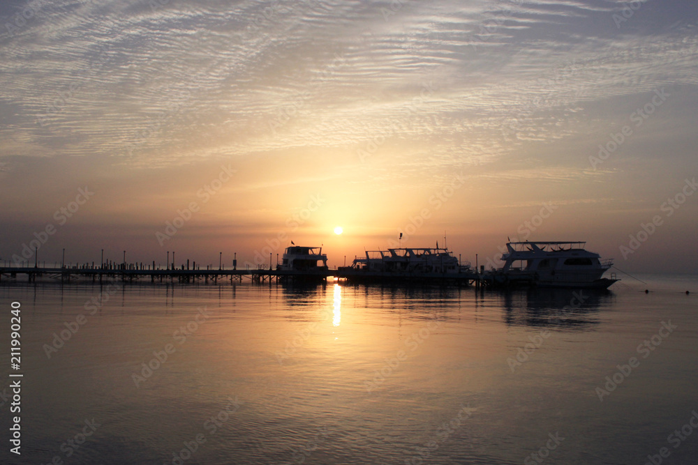Sunrise on the sea. Pier and boats on the water. Reflection of the sun in the water. Red sea, Safaga, Egypt.