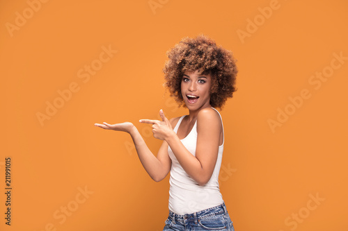 Cheerful afro woman points her fingers on yellow background.