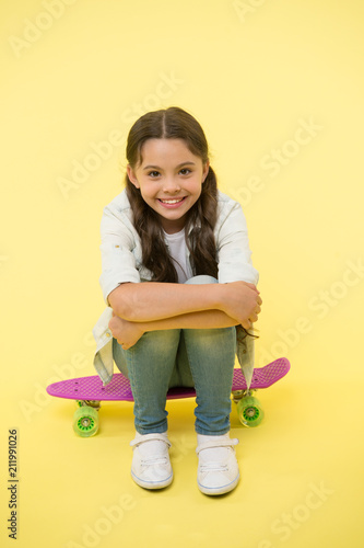 Happy girl sit on penny board on yellow background. Little child smile with long hair on skateboard. Beauty salon. Style and energy. Skills on the wheels