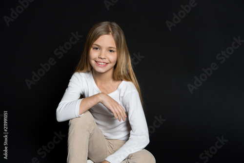 Happy child with fashion hairstyle on black background. Little girl smile with long blond hair. Beauty kid smiling with adorable look. Beauty salon. Keep calm and get your hair done