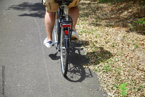 Adult man riding a bicycle. Cyclist in beige shorts. View from the back. Bike ride in the nature on a sunny summer day