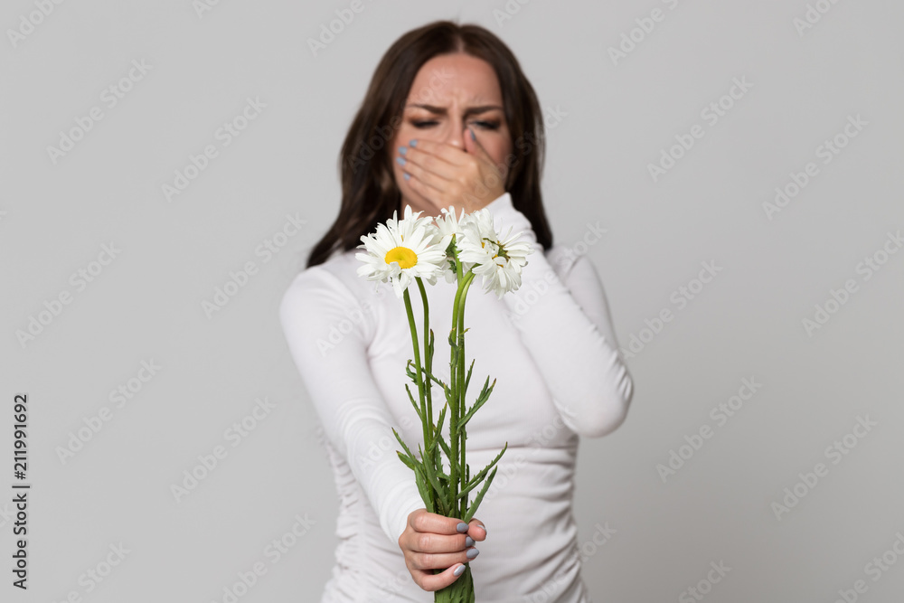 Studio portrait of brunette female covering her nose, having an allergic reaction to flowers chamomile, selective focus. Allergy. Studio portrait of brunette female covering her nose, having an allergic reaction to flowers chamomile, selective focus. Allergy.
