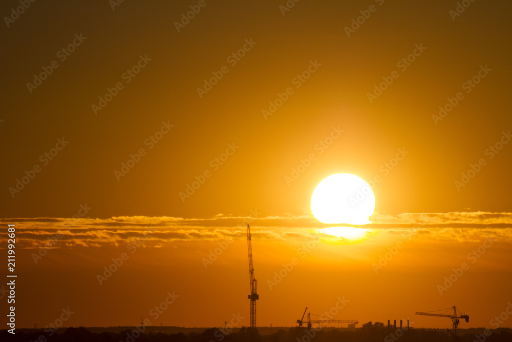 Sunset over the city. Tower crane. Industrial landscape. Bright sunset over the horizon
